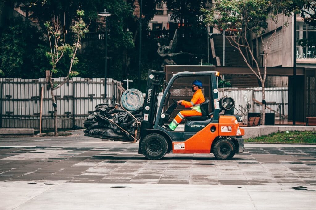 A man operates a forklift carrying rubbish in an urban environment, showcasing industrial logistics.